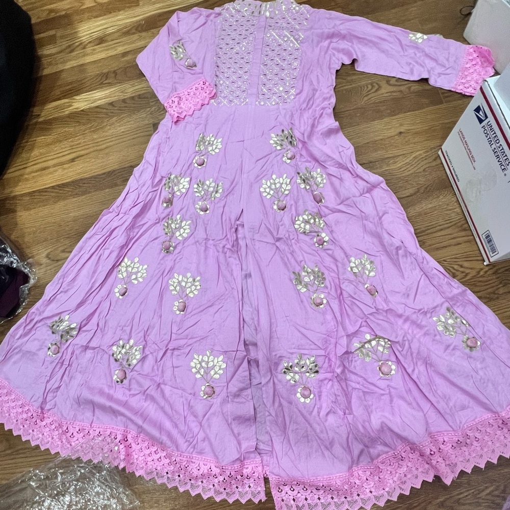 Long pink dress with golden detailing and pom poms. Slit in the middle